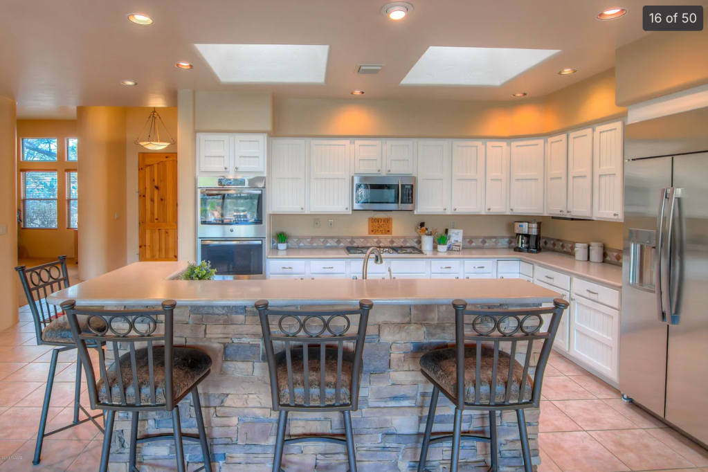 Modern kitchen with white cabinets, stone-accented island, and stainless steel appliances, featuring a large window and natural light.