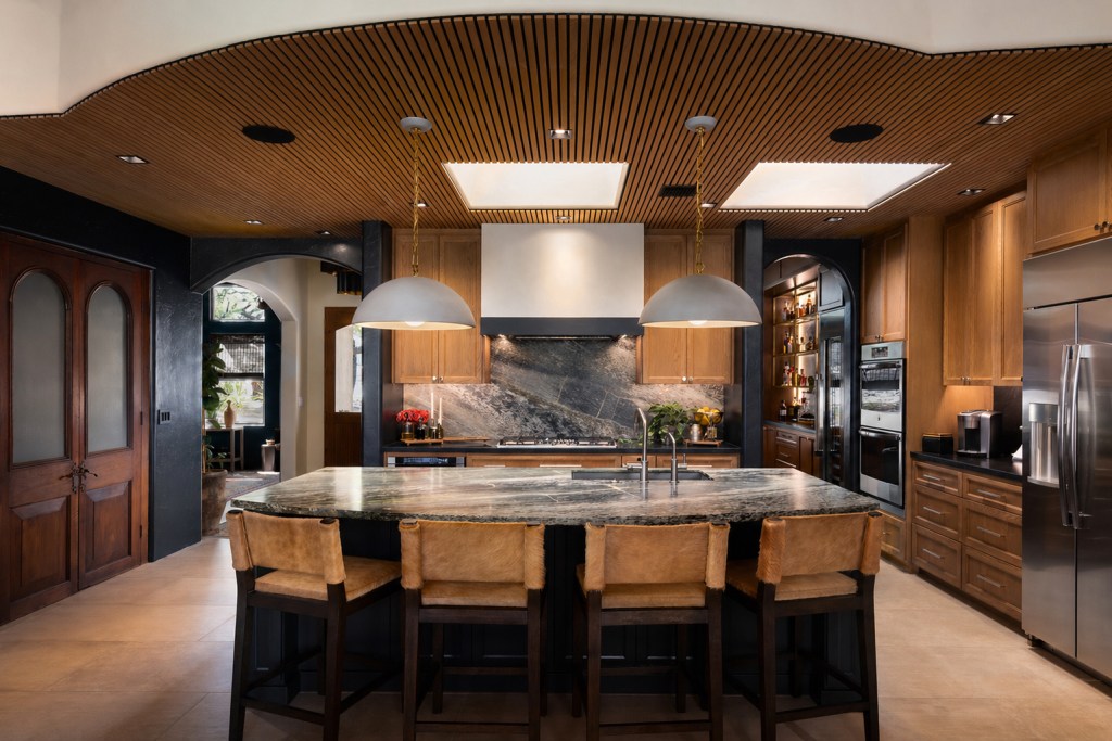 A modern kitchen featuring wooden cabinetry, an island with a granite countertop, and stylish pendant lighting. The space includes stainless steel appliances, an open layout, and a warm color palette.